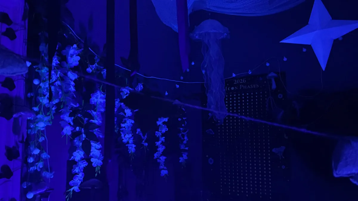 A room in blue light, hung with strings of white flowers, a jellyfish lamp and a paper star.